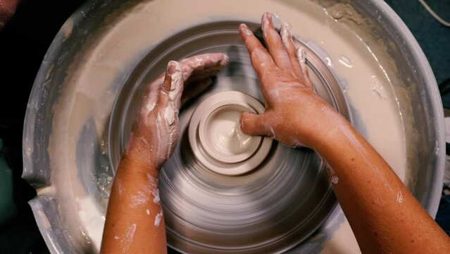 Footage shows a young potter's hands expertly molding clay on a wheel. Potter's tools play a crucial role in the creation process. Top view. Concept of handwork, art and craft