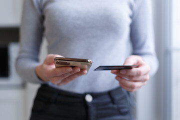 Girl shopping online with credit card. Young female person holding modern smart phone and bank card for online payment
