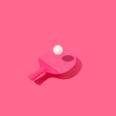 Table tennis racket and ping pong ball levitating above pink background. Minimal concept.
