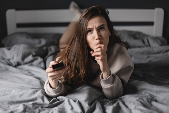 Brunette Woman Watch Tv And Hold Remote Control, And Look Shocked, Amazed, Bad News, Problems, Bad Games,  Girl Lying On The Bed And Watch Scare Movie.