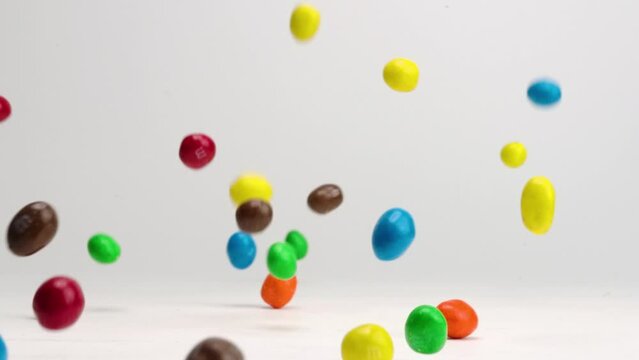 Bright colored chocolate covered peanut m and m candies bouncing around on white table top in slow motion