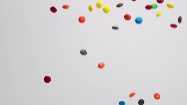 Bright multi colored chocolate covered candies falling in slow motion on white backdrop