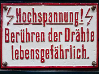 German High Voltage warning sign : "Hochspannung! Berühren der Drähte lebensgefährlich." means "High voltage! Touching of wires is life threatening." (translation) . Old white lacquered sign red text 