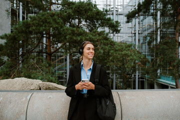 Young woman using headphones and mobile phone while standing outdoors