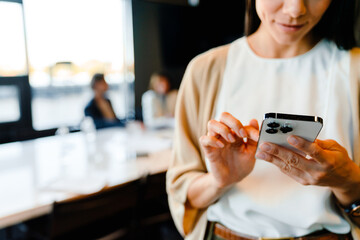 Hispanic young woman smiling and using cellphone during offline meeting