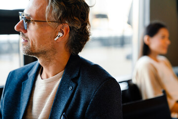 Mature manager in earphones looking in window during offline meeting