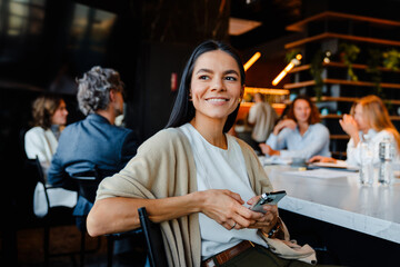 Hispanic young woman smiling and using cellphone during offline meeting