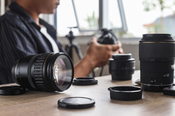 Various of lenses on wooden table against blurry background of photographer setting professional camera - obrazy, fototapety, plakaty