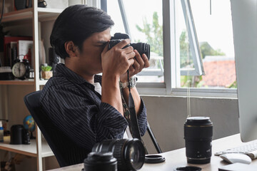 Young man photographer sitting and take a shoot with professional camera at home office studio. 