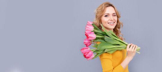 winking cheerful lady hold flowers for spring holiday on grey background. Woman isolated face portrait, banner with mock up copy space.