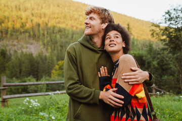 Multinational couple smiling and hugging while walking in forest