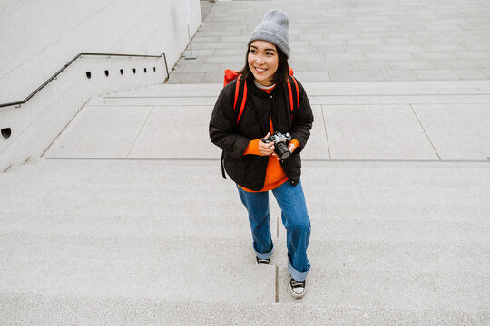 Cheerful asian woman taking pictures with vintage camera while climbing the stairs