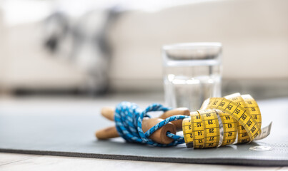 A skipping rope, a tape measure and a glass of water on a mat at home in the living room. Concept of healthy lifestyle