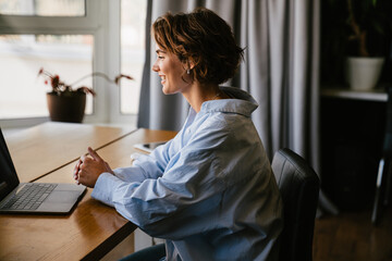 Smiling business woman making video call via laptop while sitting in modern office