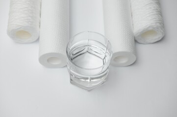 A glass of drink water and filter cartridges at white background