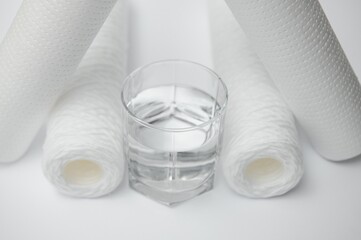 Water filters. Carbon cartridges and a glass on a white background. Household filtration system