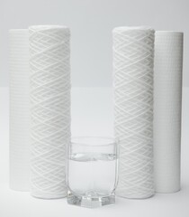 A glass of drink water and filter cartridges at white background