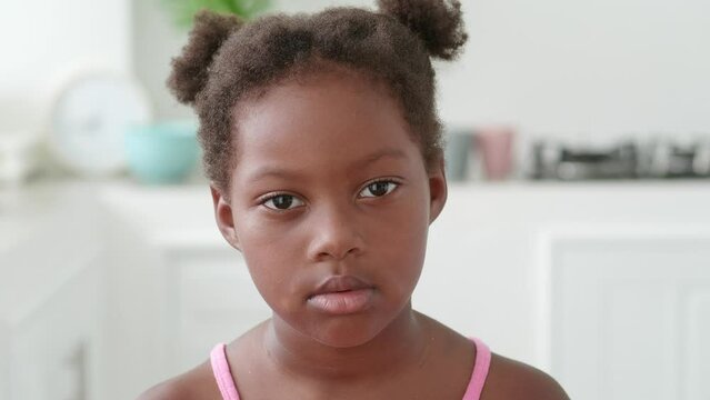 Portrait of sad kid against the backdrop of apartment. sad kid with dark-eyedstares piercingly straight into camera. sad kid female standing in bright room concept of negative emotions