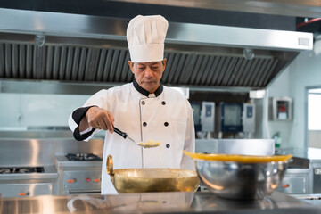 Professional Asian chef working in the restaurant kitchen. Chef stirring soup with spoon in the...