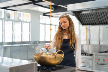 Child girl chef cooking in the restaurant kitchen. Child girl stirring soup with spoon in the...