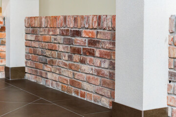 Detail of the corner baseboard on the wall and granite tiles on the floor. The wall is lined with decorative bricks, white columns and brown baseboards. Interior design in an office building.