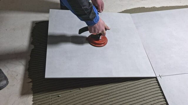 Tiler worker placing or tiling gray ceramic tile in the position over adhesive glue with lash tile leveling system, renovation or recontruction, concept of building