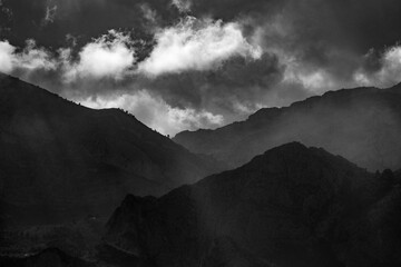 dramatic sky over rugged mountain silhouettes in black and white
