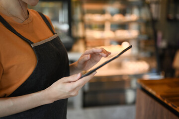 Cropped shot of female waitresses in apron using tablet and checking inventory in modern coffee shop