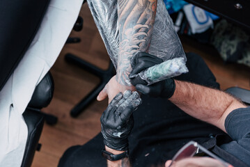 Top view of tattoo artist working on process on forearm with white ink. Detailed hands with black...