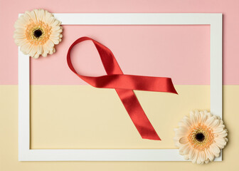 Red ribbon of the Cancer Day on a pink and beige background. Women's and men's health.
