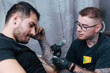 Tatooist tattooing client cover up on forearm, arm. Young men.Tattoo master on studio. Small...