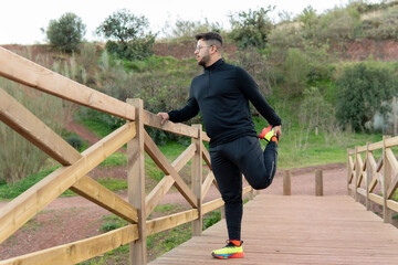 Young adult in the countryside stretching on a wooden bridge for outdoor sports.