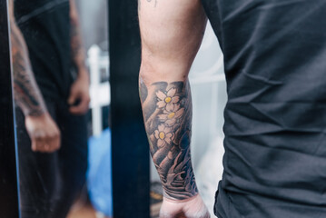 Young man looking at mirror his new tattoo on forearm. Cover up. Professional tattoo artist in...
