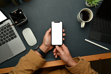 Overhead view of businessman hands holding smart phone while sitting front of laptop at workstation