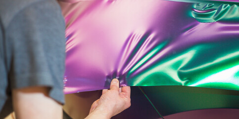 A specialist in wrapping a car with chameleon-colored vinyl film in the process of work. Car wrapping specialists cover the car with vinyl sheet or film. Selective focus.