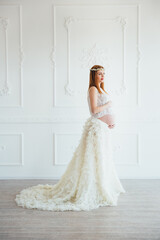 red-haired pregnant young girl in a white dress near the white wall