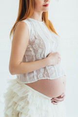 red-haired pregnant young girl in a white dress near the white wall