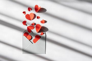 background for valentine's day. red paper hearts fly out of the envelope with a beautiful shadow and light. flat lay