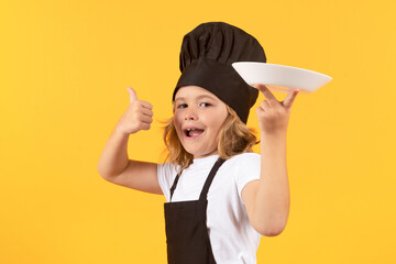 Funny child cook with cooking plate. Kid chef cook prepares food on isolated studio background. Kids cooking. Teen boy with apron and chef hat preparing a healthy meal.