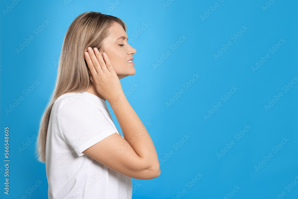 Wall mural Young woman suffering from ear pain on light blue background. Space for text