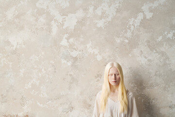 Young serene albino woman in white pullover keeping her eyes closed while standing by fair marble...