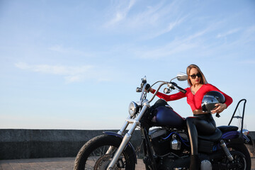 Fototapeta na wymiar Beautiful young woman with helmet sitting on motorcycle outdoors