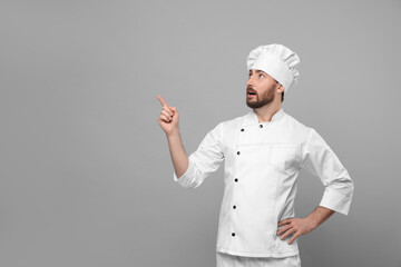 Mature chef pointing at something on grey background, space for text
