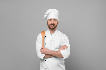Smiling mature chef with spoon on grey background, space for text