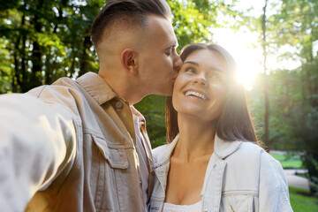 Fototapeta premium Affectionate young couple kissing and taking selfie in park