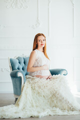 red-haired pregnant young girl in a blue armchair