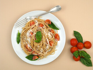 Plate with whole grain spaghetti pasta with cherry tomatoes, basil and parmesan cheese.