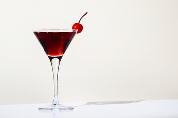 Black Manhattan cocktail with whiskey and red vermouth garnished with maraschino cocktail cherry in martini glass. Beige background, hard light