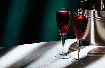Kir Royale alcoholic cocktail with blackcurrant liqueur, prosecco and cocktail cherry. Dark green background, hard light and shadow pattern