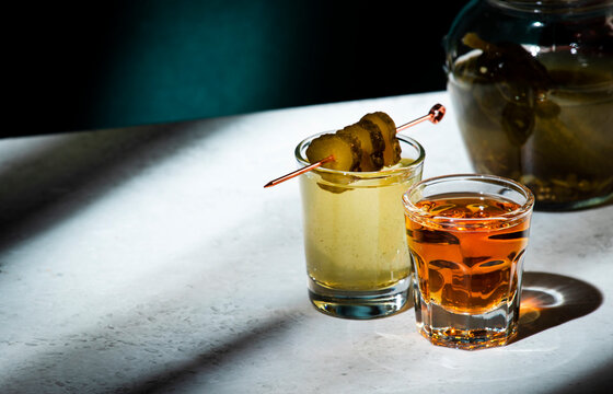 Pickleback, alcoholic cocktail made from cucumber pickle and whiskey in small shot glasses. Hard light and shadows